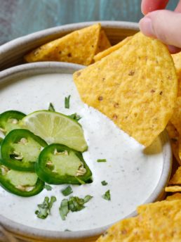 tortilla chip being dipped into a bowl of creamy ranch dip topped with jalapenos