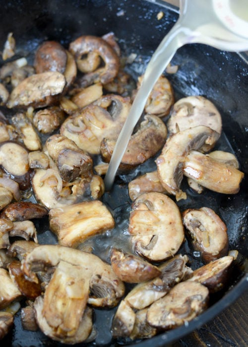 chicken broth and white wine being poured into a cast iron skillet with sauteed mushrooms, shallots, and garlic