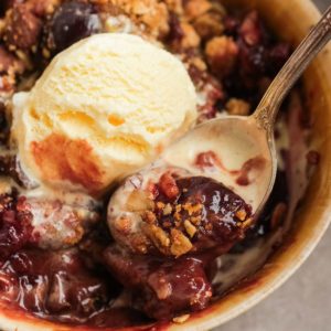 A spoonful of a cherry crisp with vanilla ice cream