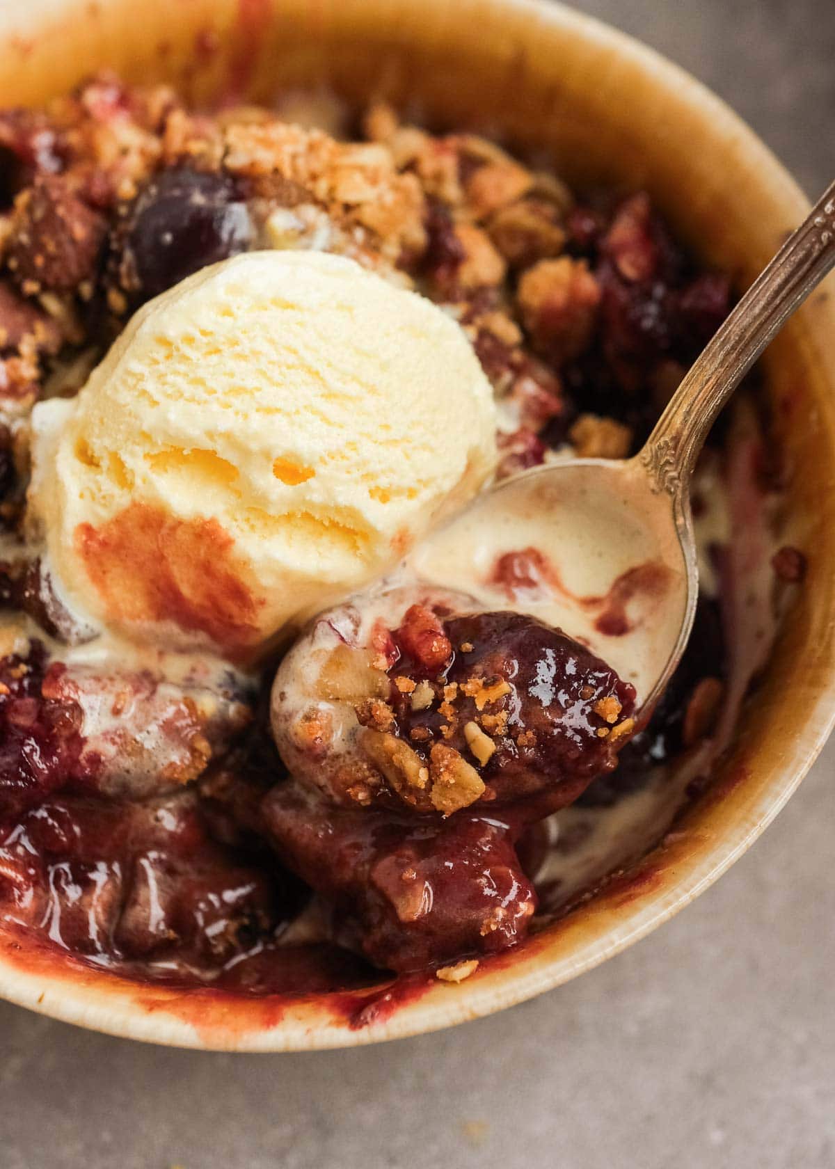 A spoonful of a cherry crisp with vanilla ice cream