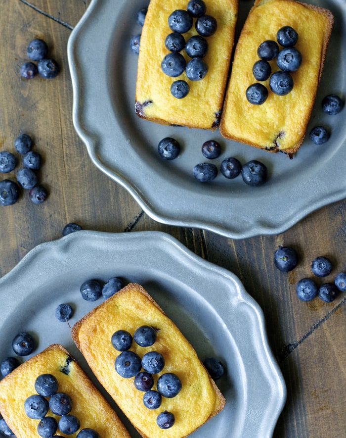 Overhead view of mini blueberry cornmeal cake loaves on gray plates. 