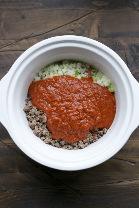 marinara sauce poured over ground beef, vegetables, and beans in a slow cooker