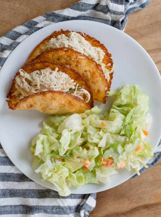 ranch seasoning chicken in two cheese taco shells with a side salad on a white plate. 