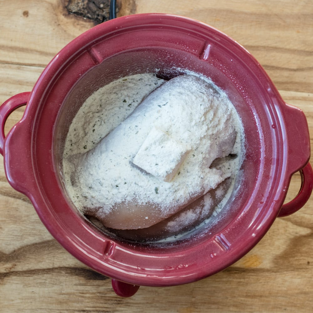 ranch seasoning mix sprinkled over chicken and butter in a slow cooker