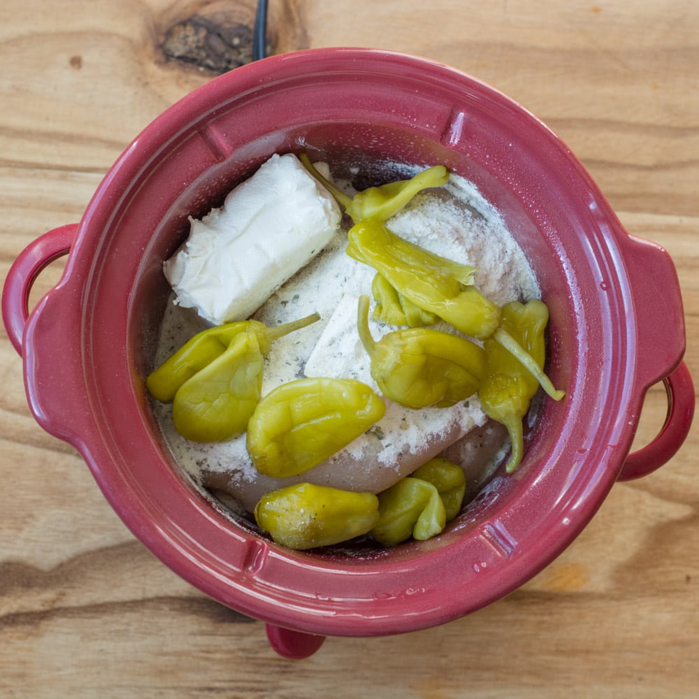 cream cheese and pepperoncini peppers added to the ranch seasoning, butter, and chicken breasts in a slow cooker for ranch chicken.