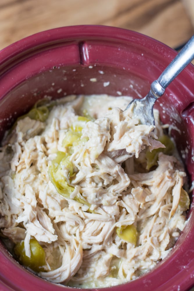 a fork grabbing a big bite of creamy ranch chicken from a slow cooker