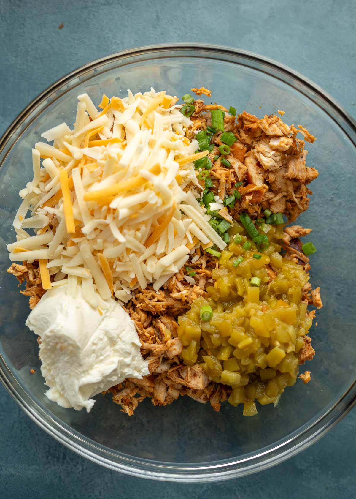 A bowl of chicken, cheese, green chiles, cream cheese, and green onions in a bowl.