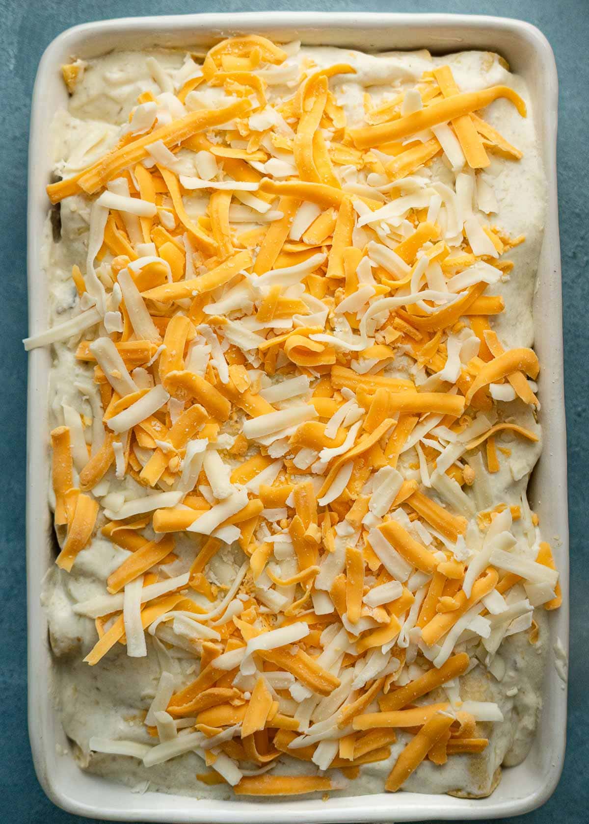 sour cream chicken enchiladas topped with cheese in a casserole dish