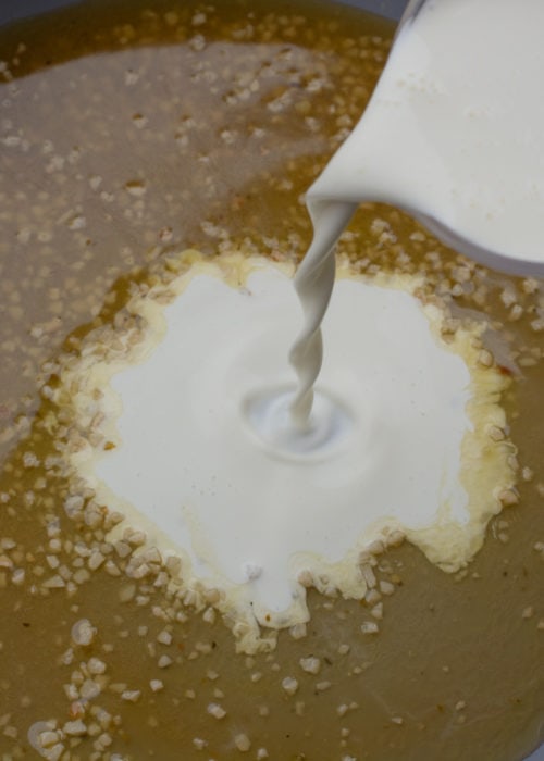 heavy cream being poured into a white wine garlic reduction