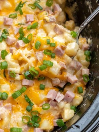 Cheesy Hashbrown Casserole is the perfect comfort food! Frozen hashbrowns are paired with sour cream, cheddar cheese, and ham to make the ultimate side dish! This simple potato recipe requires no prep work and can be made in the crock pot or oven!