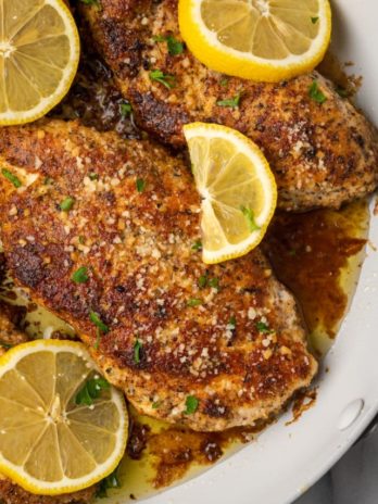 Lemon chicken in skillet with butter sauce, lemon slices, and parsley garnish