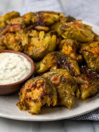 Crispy smashed Brussels sprouts on plate with bowl of lemon aioli