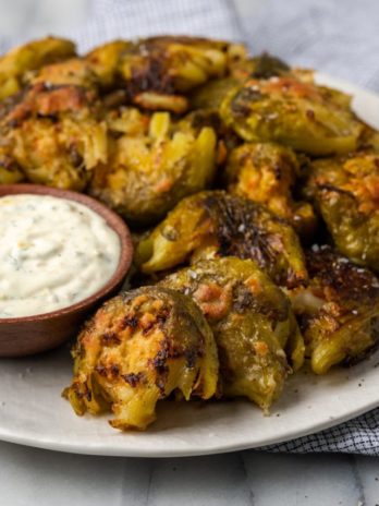 Crispy smashed Brussels sprouts on plate with bowl of lemon aioli