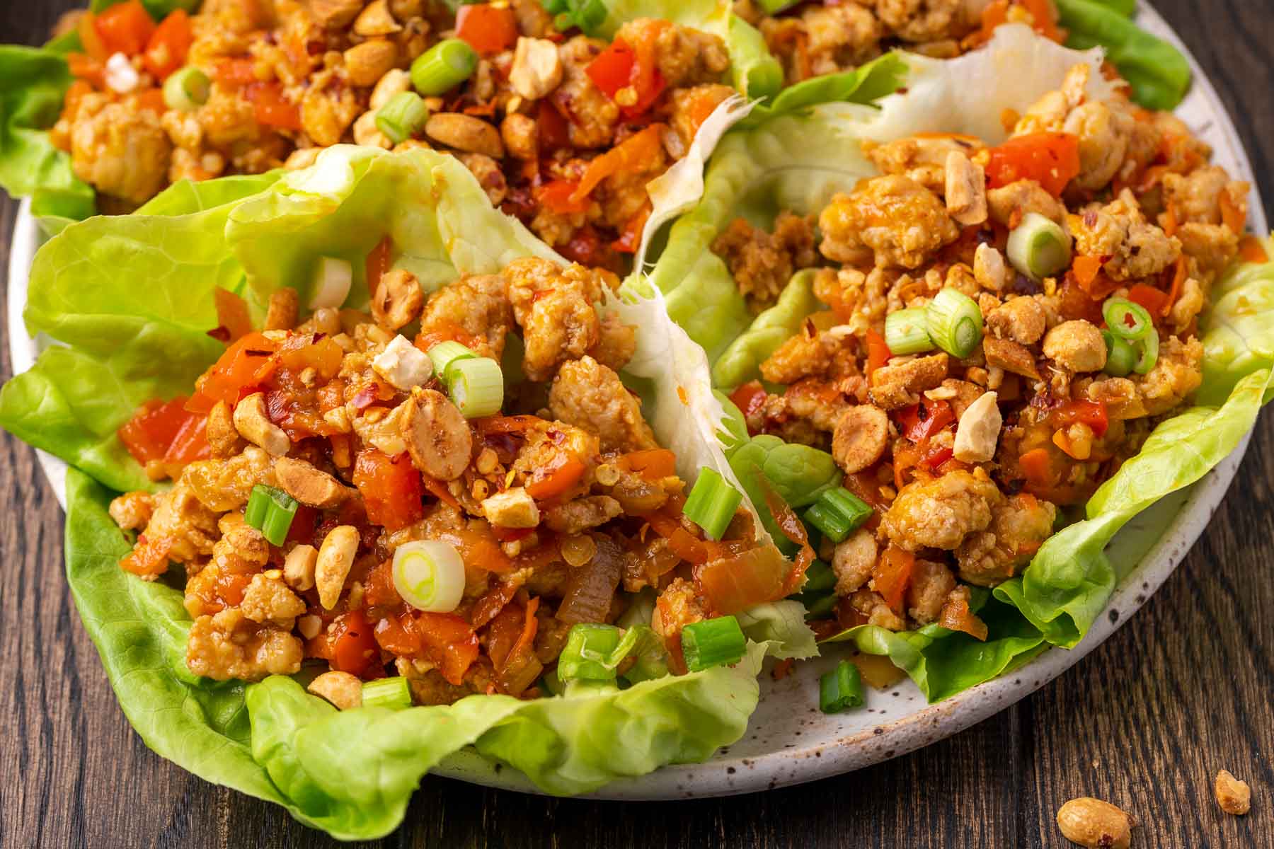 horizontal image showing several chicken lettuce wraps full of ground chicken, shredded veggies, and a delicious sesame sauce