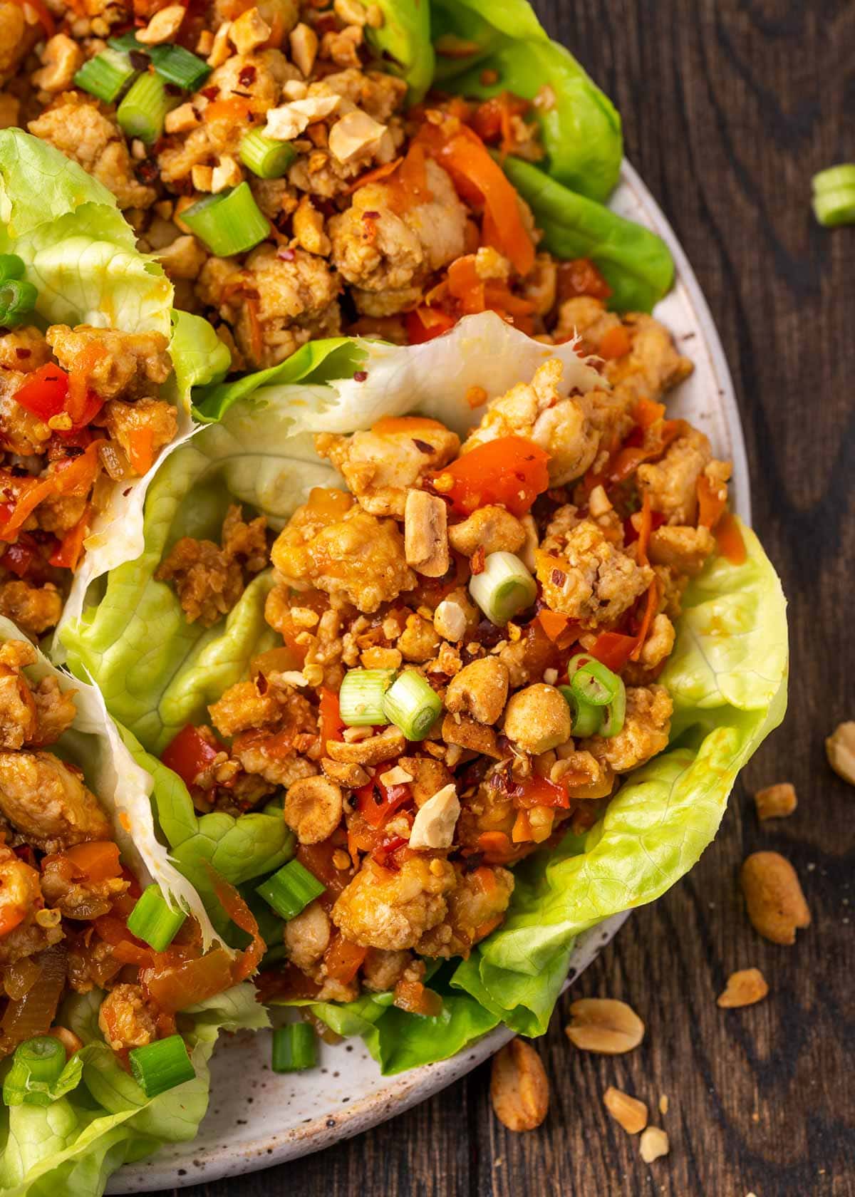 a white plate loaded with several lettuce wraps full of juicy chicken and veggies covered in a sesame soy sauce