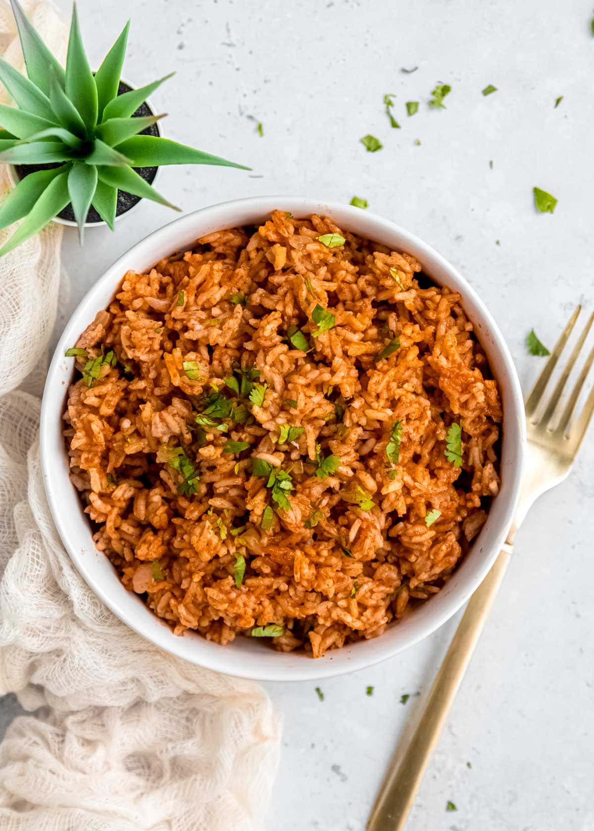 overhead shot showing a white bowl full of Mexican rice topped with fresh herbs on a white counter top