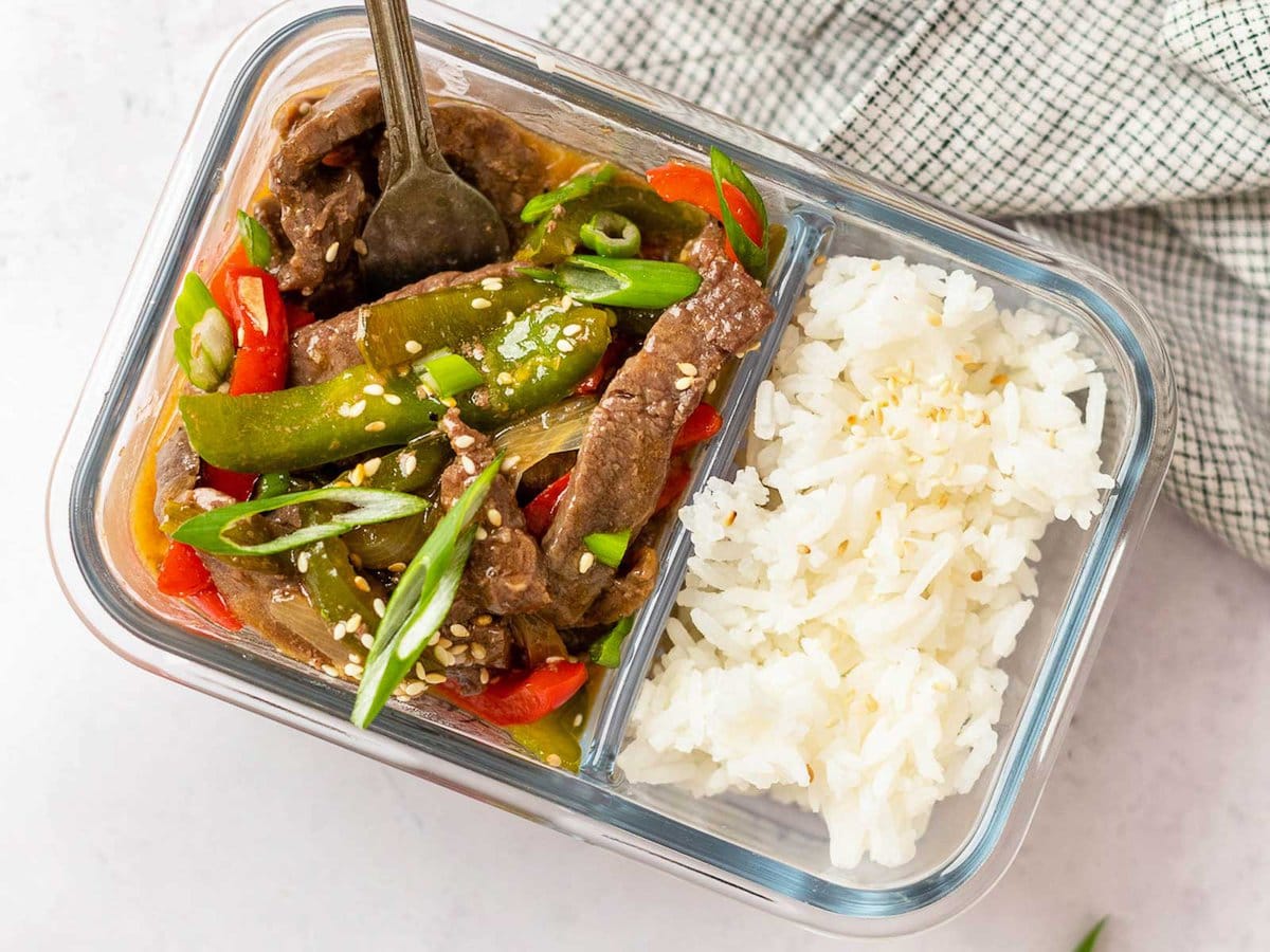 horizontal image showing a meal prep container filled with pepper steak and white rice