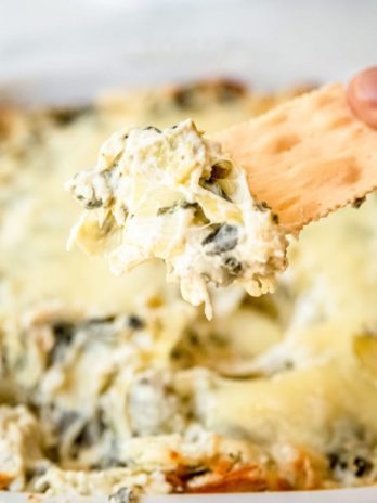 a hand holding a cracker with easy baked spinach artichoke dip