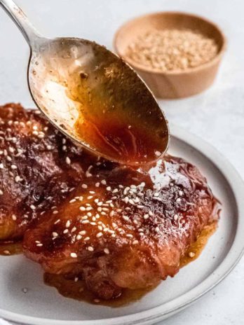 sauce being spooned onto asian chicken thighs on a plate