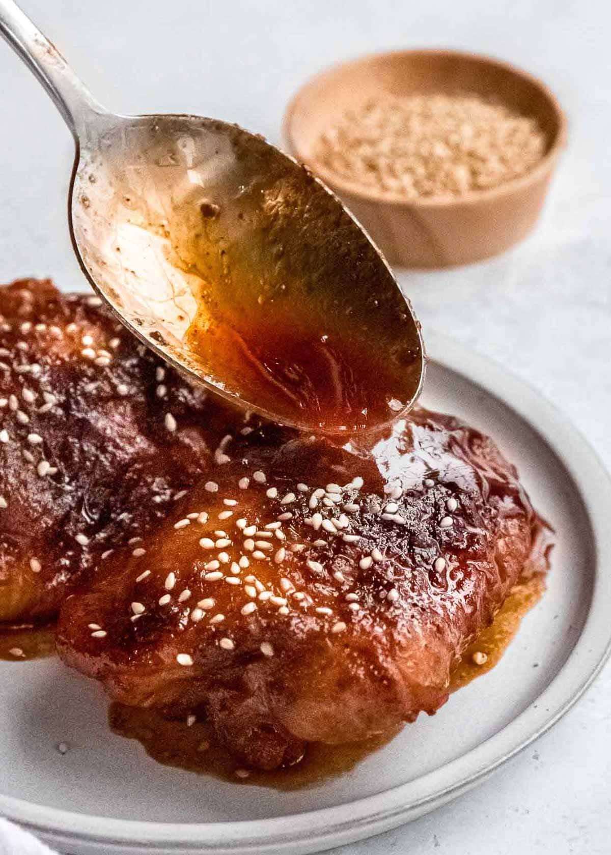 sauce being spooned onto asian chicken thighs on a plate