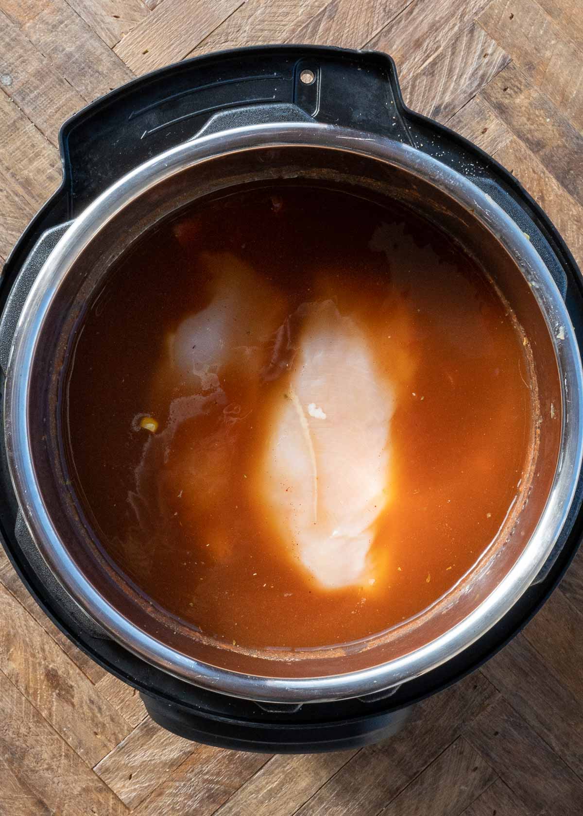 raw chicken being placed in instant pot with chicken tortilla soup ingredients