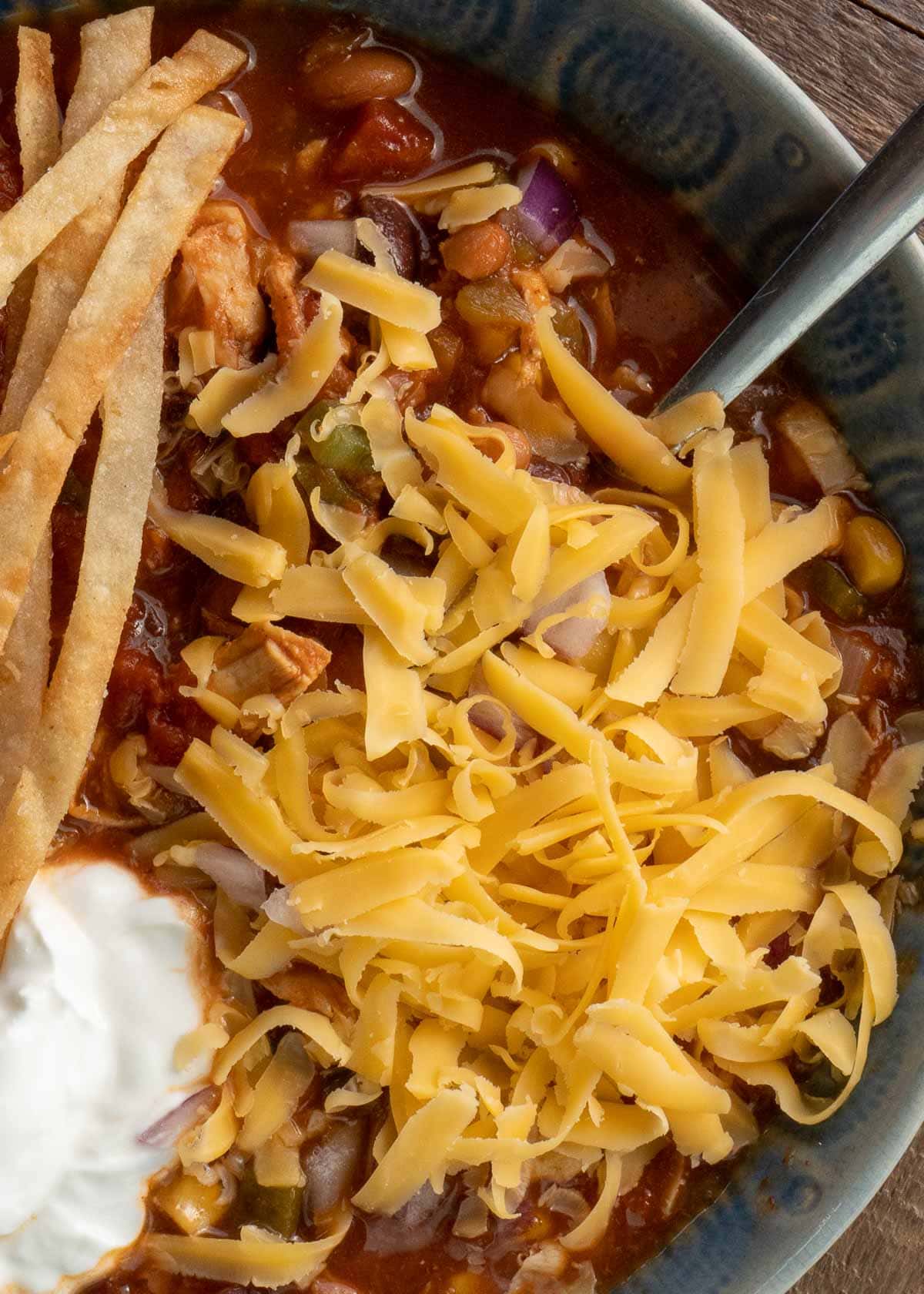 closeup view of melty cheese atop Instant Pot Chicken Tortilla Soup in a blue bowl with sour cream and tortilla chips