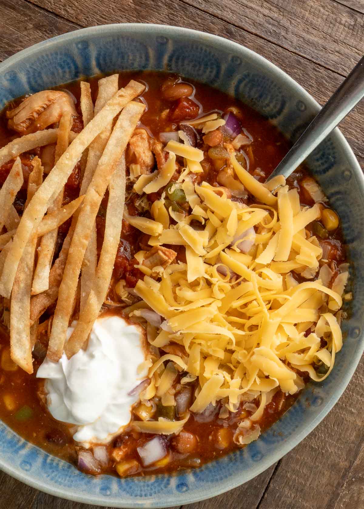 a blue bowl filled with instant pot chicken tortilla soup, garnished with sour cream, shredded cheese, and crispy tortilla strips