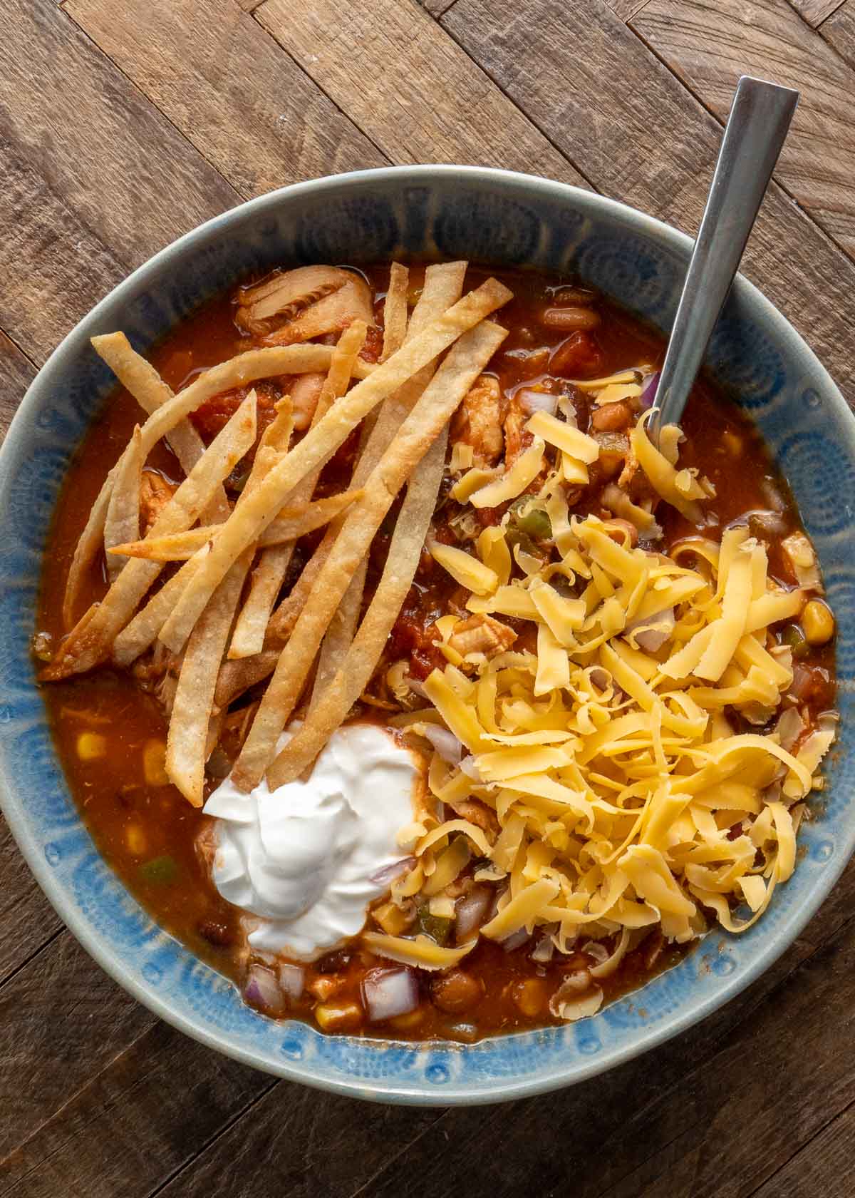 overhead shot of a blue bowl full of chicken tortilla soup straight from the instant pot; soup is garnished with crispy tortilla strips, a dollop of sour cream, and shredded cheddar cheese