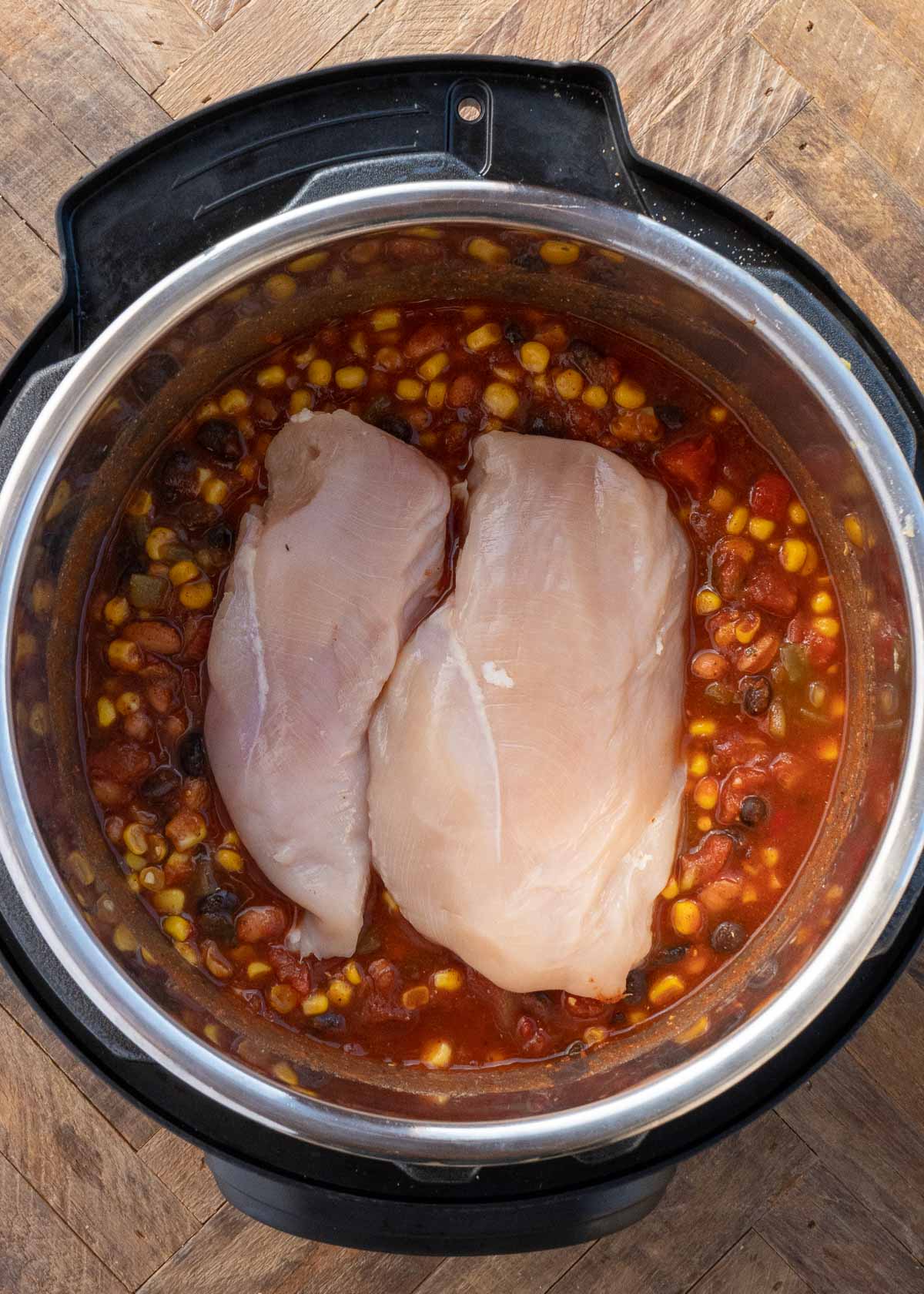 raw chicken being placed in instant pot with chicken tortilla soup ingredients