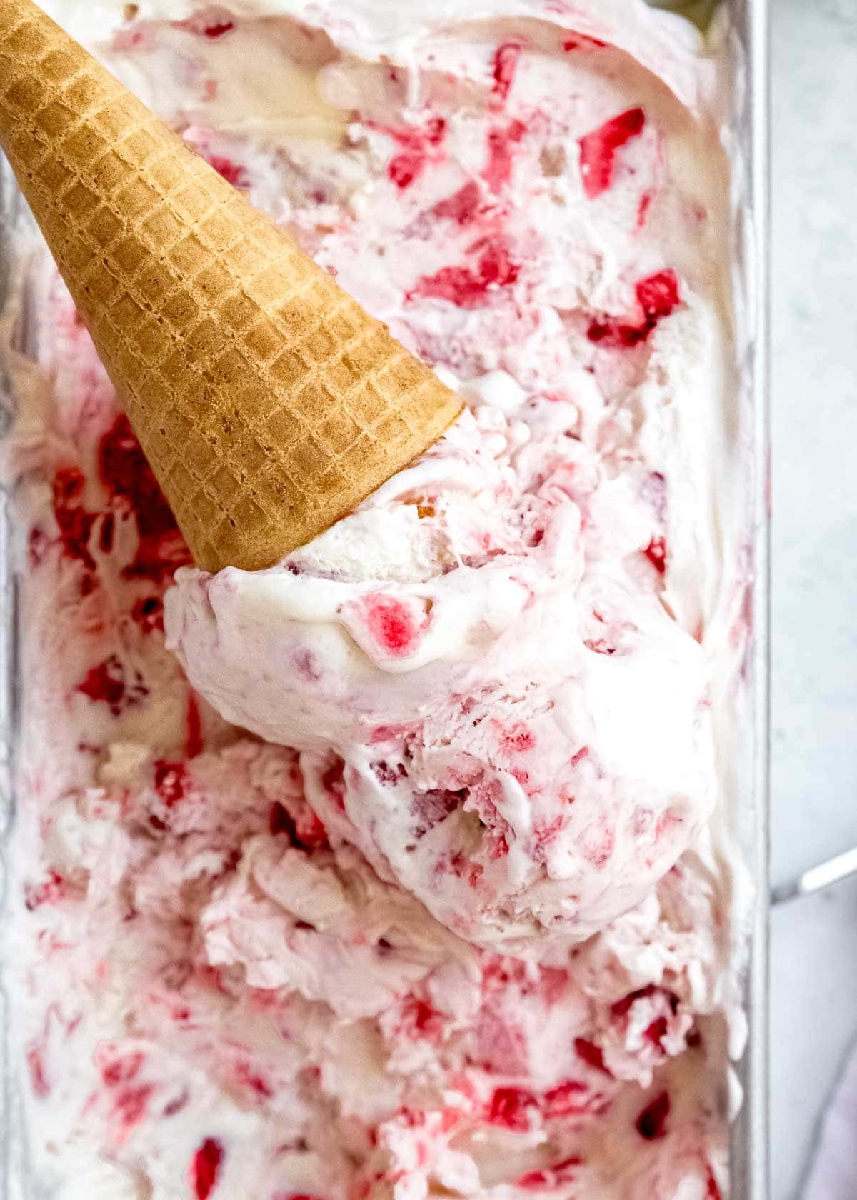 no churn strawberry ice cream scooped into a waffle cone on top of the batch of homemade ice cream