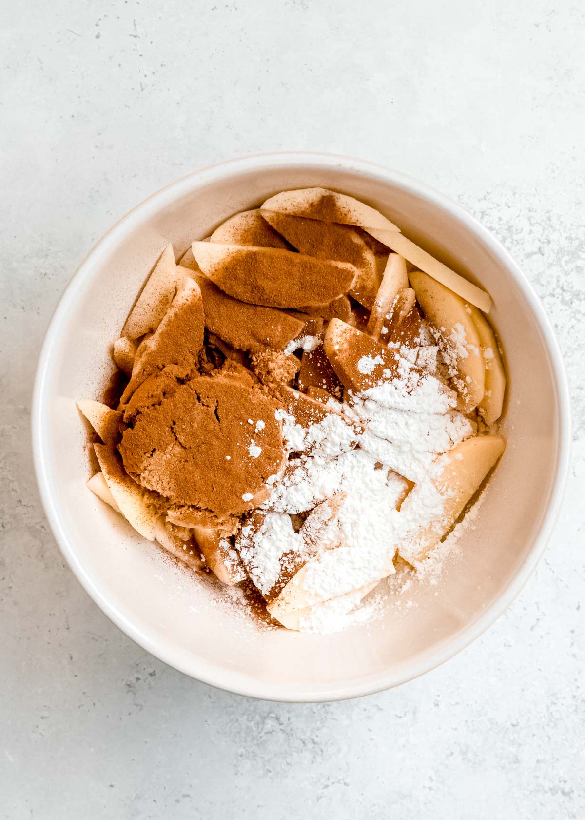 sugar, cornstarch, and cinnamon with apples in a bowl