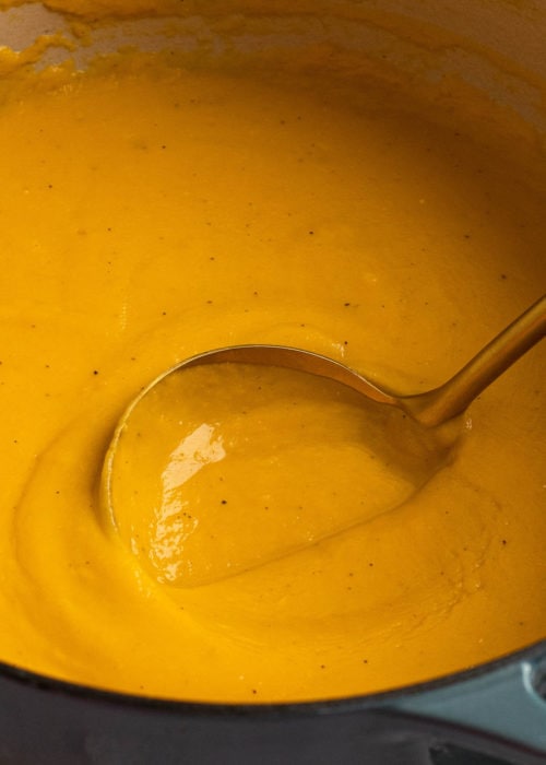 closeup image showing a large ladle spooning out a big scoop of creamy butternut squash soup