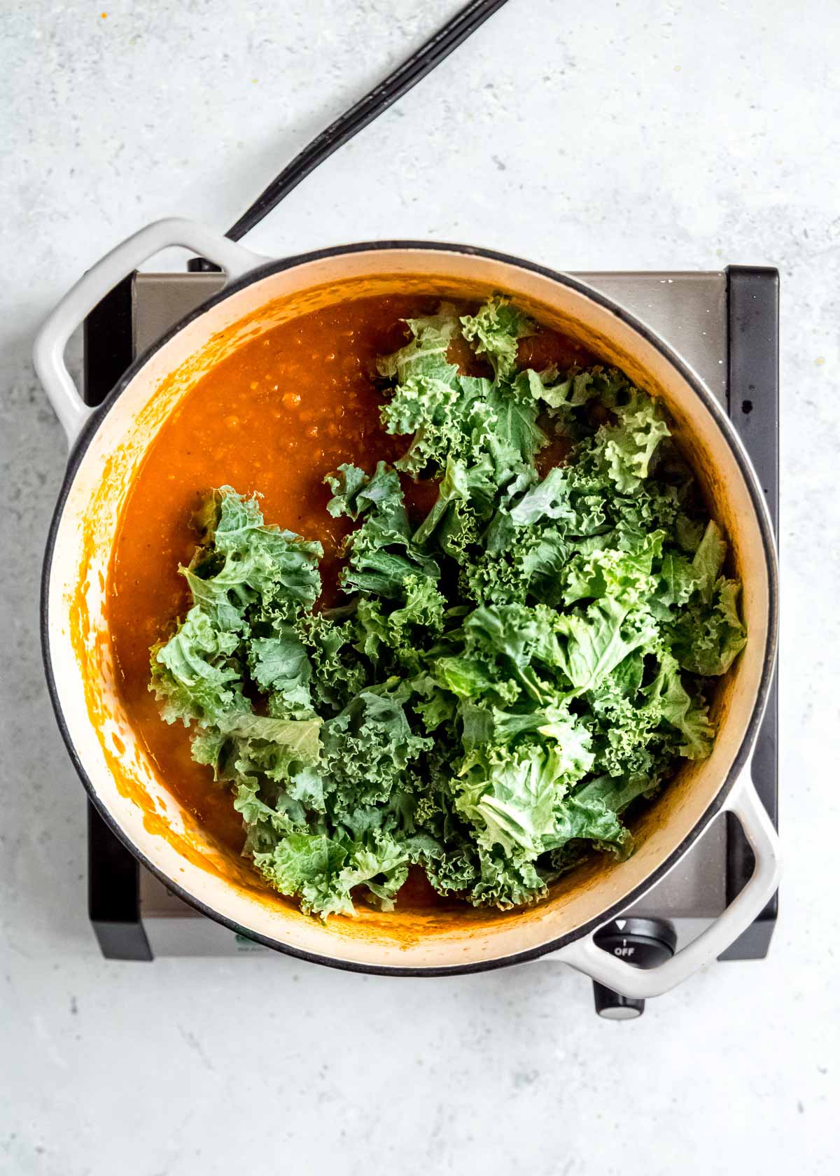 overhead shot of kale being added to lentil soup