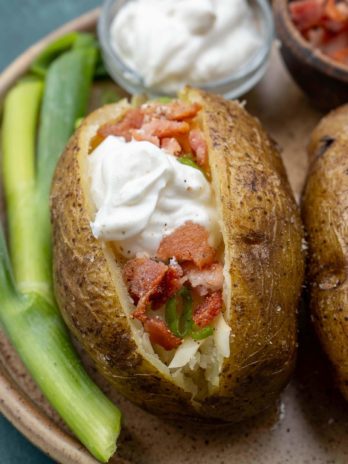 close up of loaded instant pot baked potato on brown plate