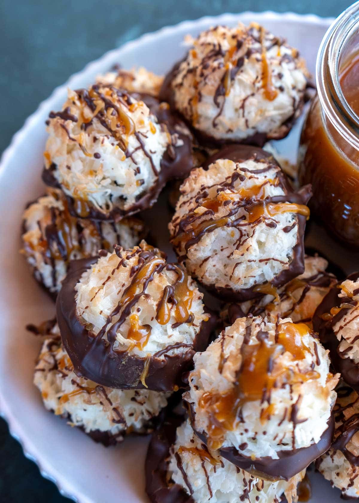 a white plate full of coconut macaroons dipped in sugar-free chocolate and topped with keto caramel sauce