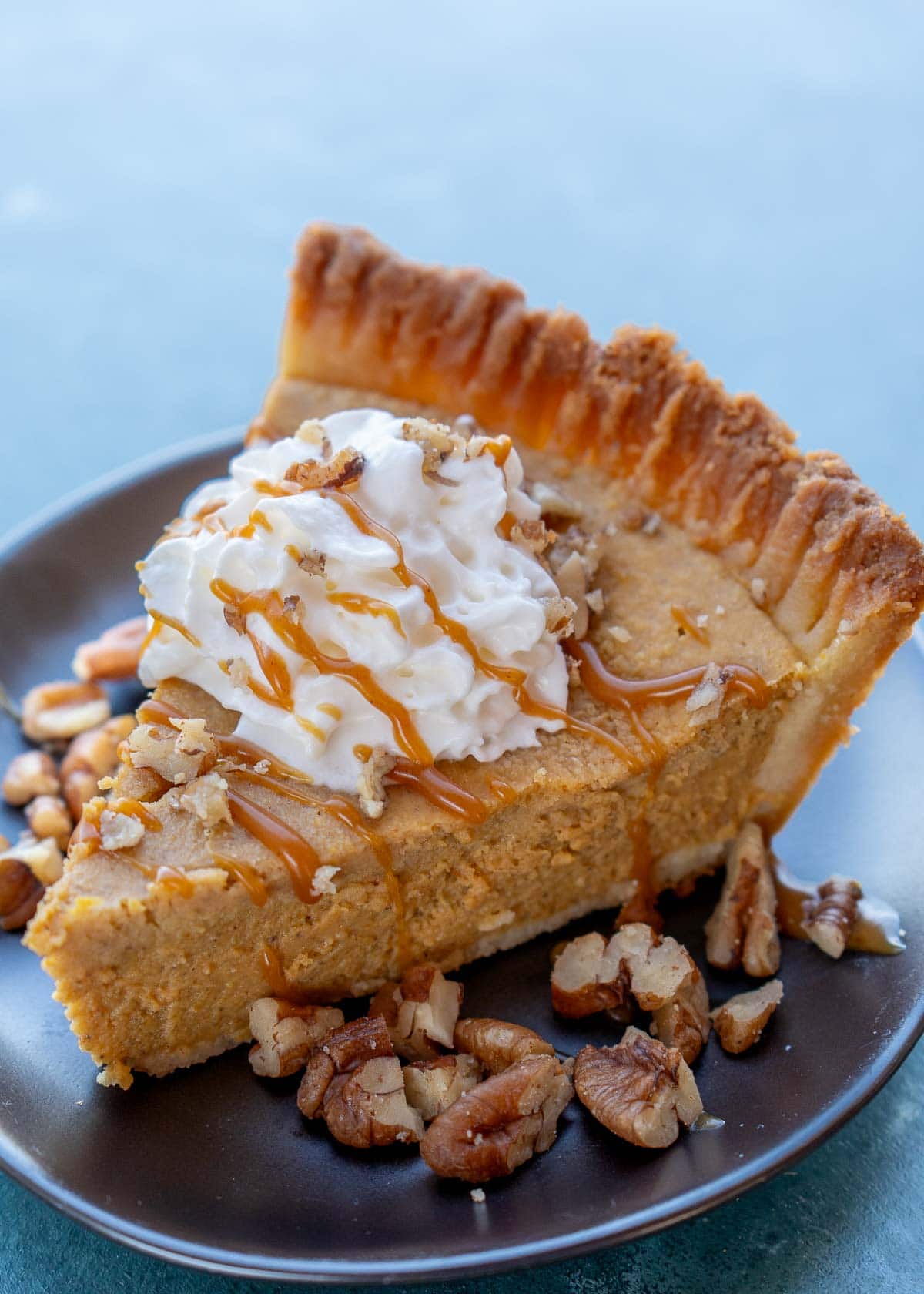 the perfect slice of a gluten-free pumpkin pie topped with crumbled pecans, keto caramel sauce, and whipped cream