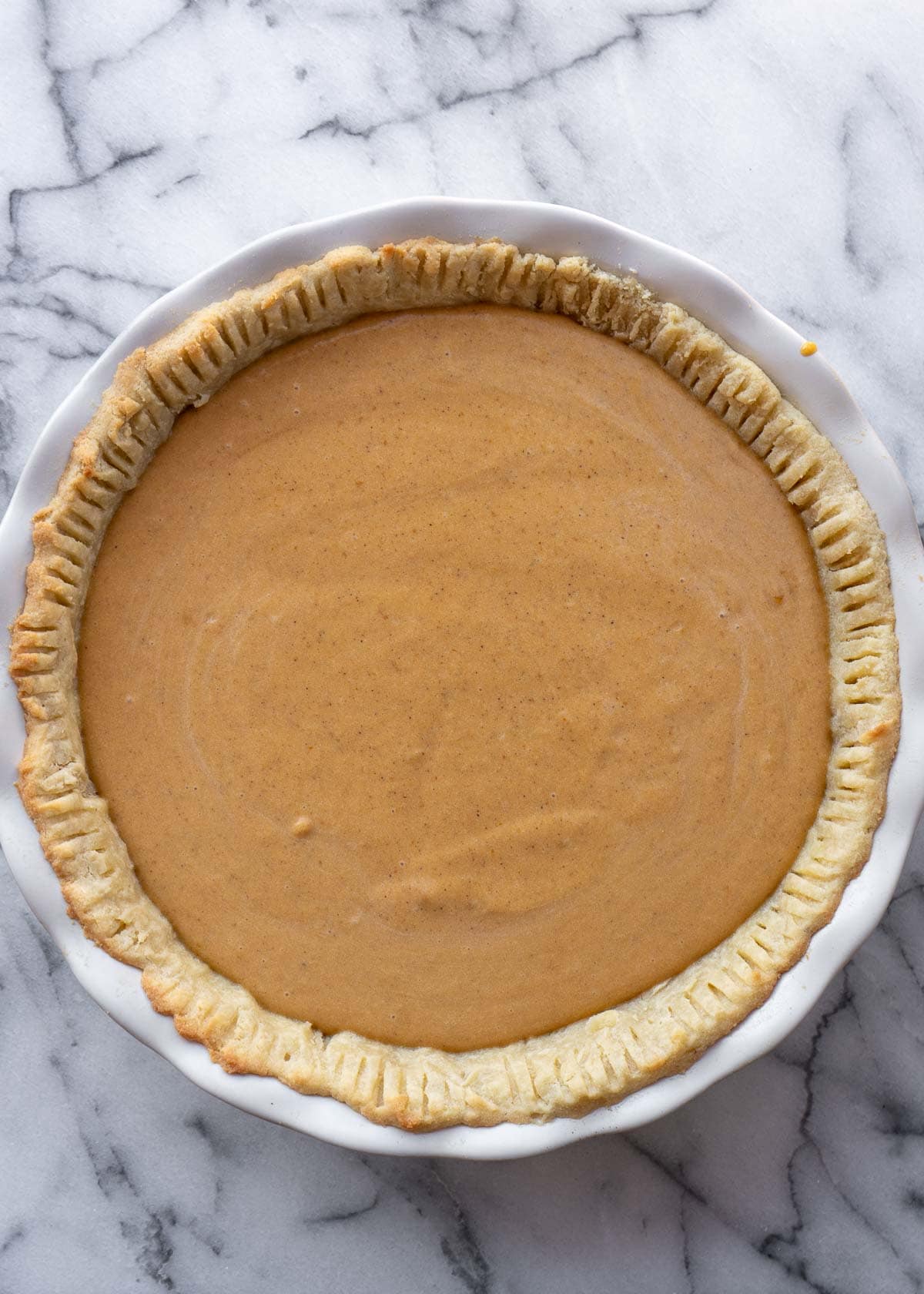 baked gluten-free pumpkin pie in a white pie pan on a marble countertop ready for Thanksgiving