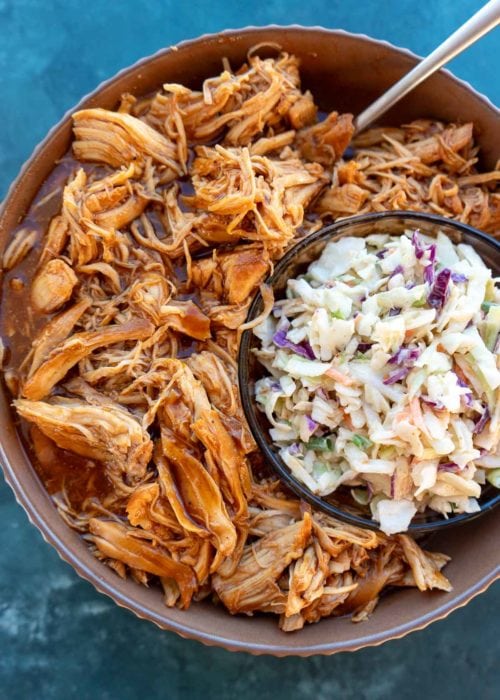 overhead shot showing juicy chicken covered in bbq sauce and shredded. a bowl of keto slaw is beside the chicken