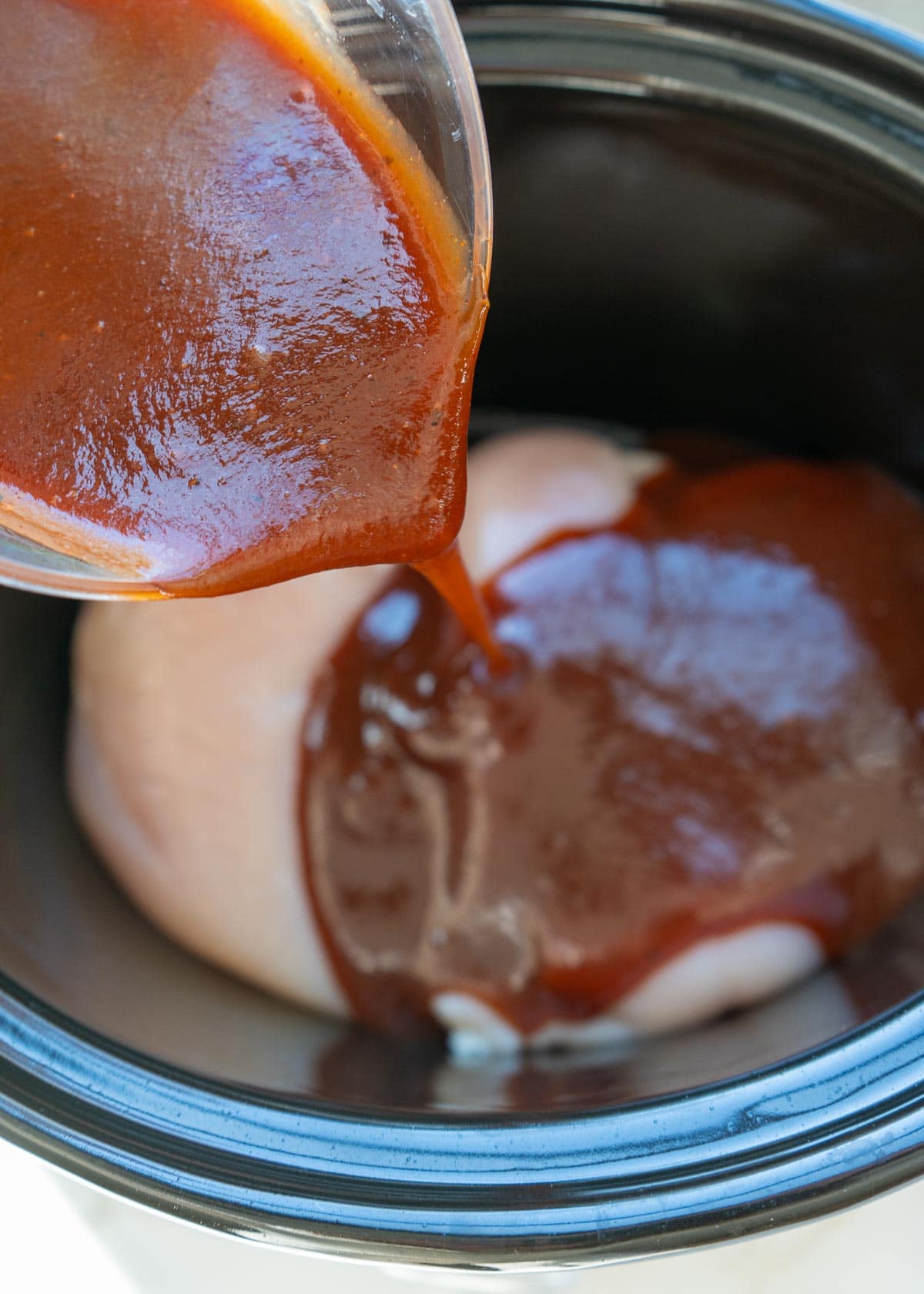 overhead image of bbq sauce being added to chicken in crockpot