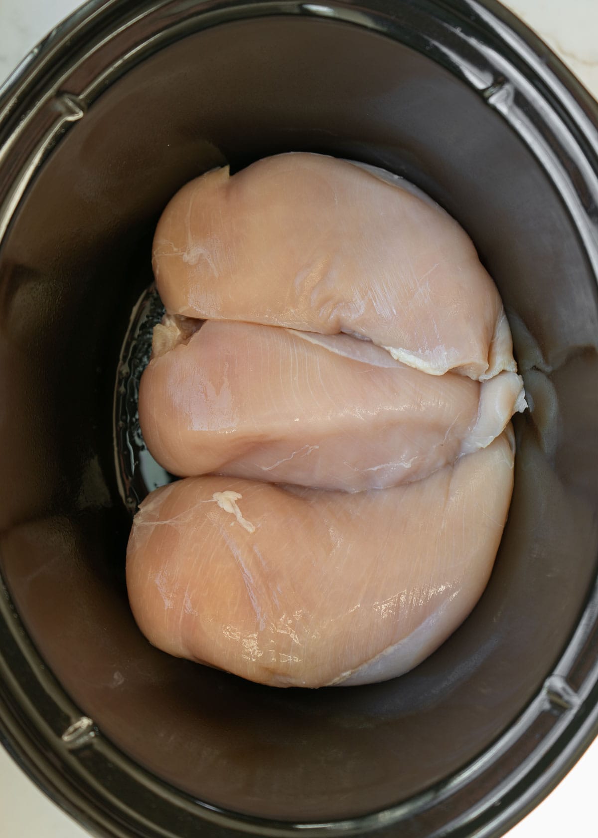 overhead image of raw chicken in crockpot