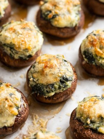 cheesy spinach stuffed mushrooms on a parchment paper lined baking pan