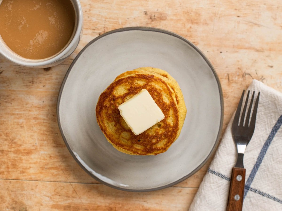 overhead shot showing a stack of almond flour pancakes on a plate with a napkin and fork on one side, a cup of coffee on the other side