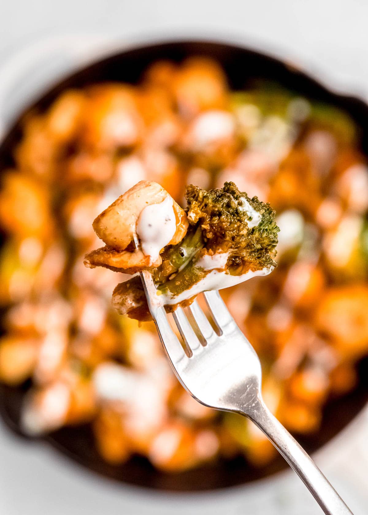 bite of buffalo chicken and broccoli on fork with buffalo chicken skillet in background