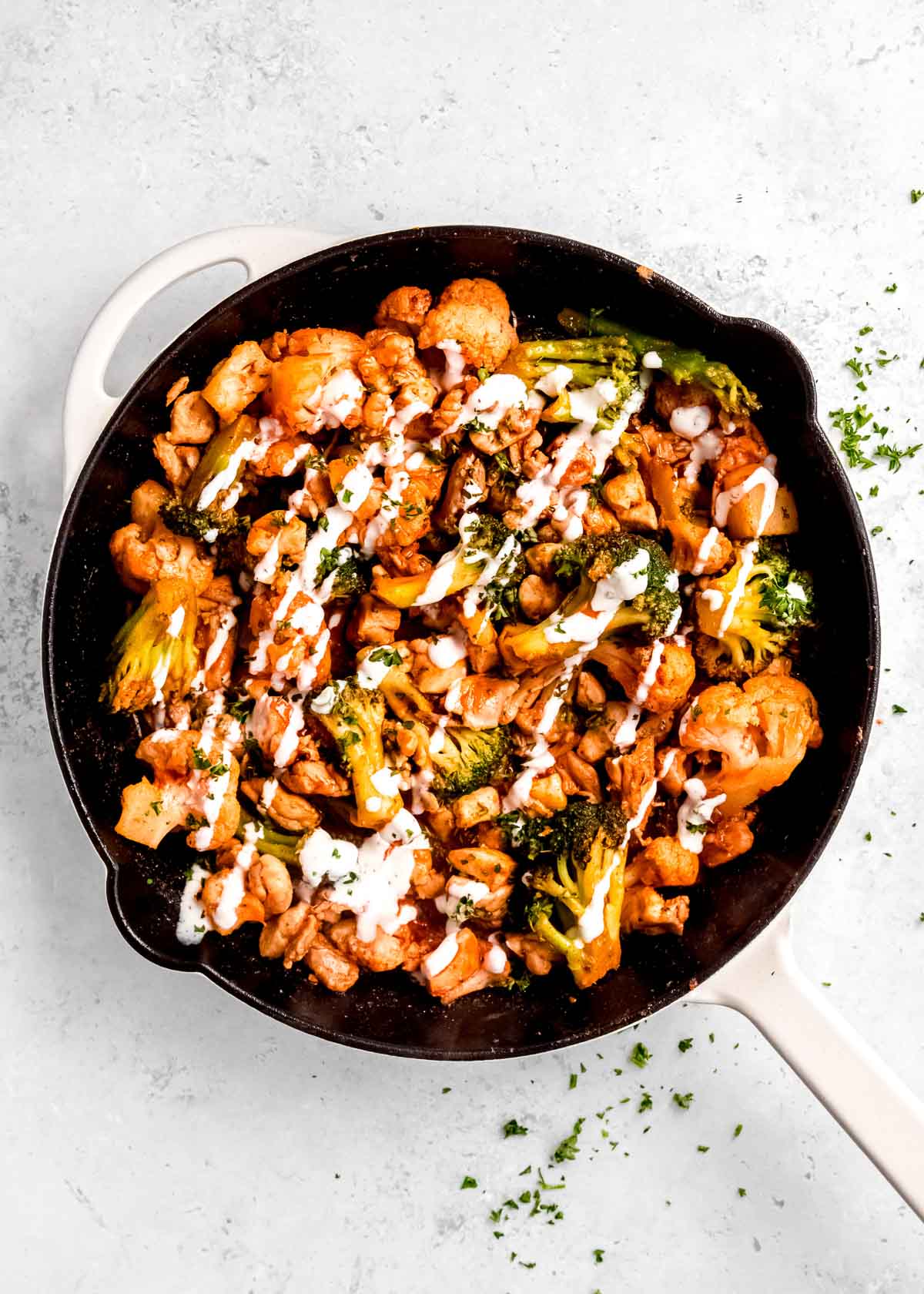 overhead image of ranch dressing being drizzled on buffalo chicken skillet  