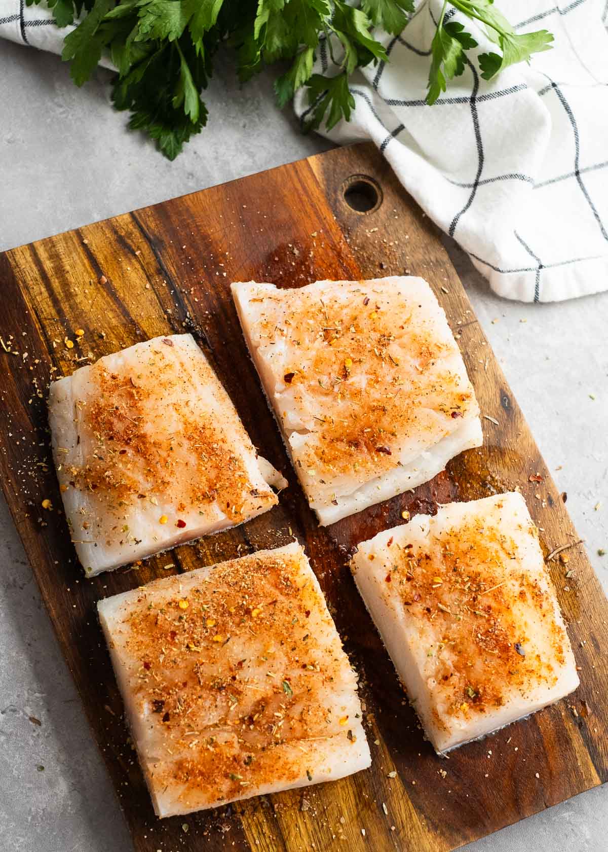 Four raw seasoned cod filets on wooden cutting board