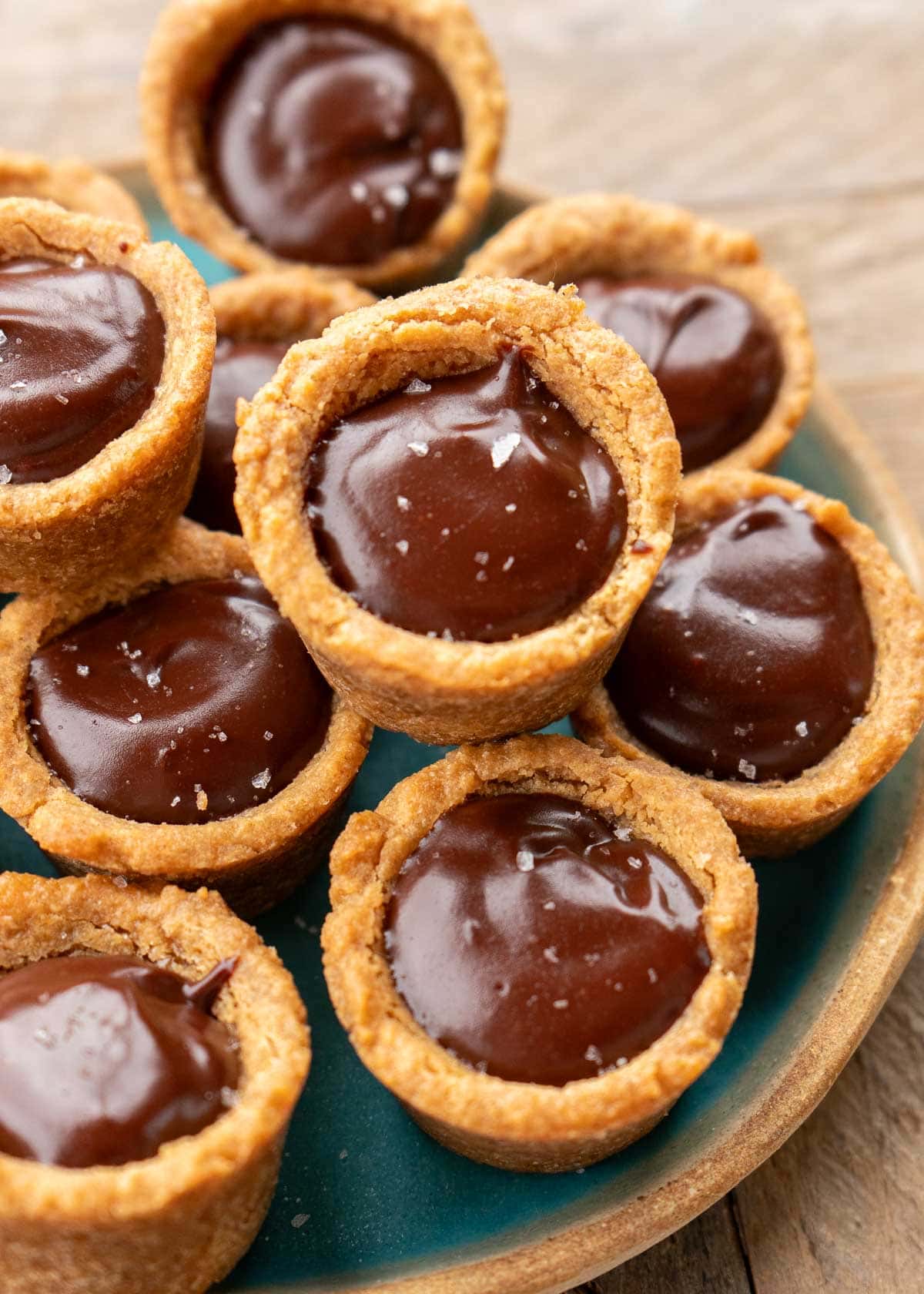 a teal plate topped with several chocolate peanut butter cookie cups, sprinkled with sea salt