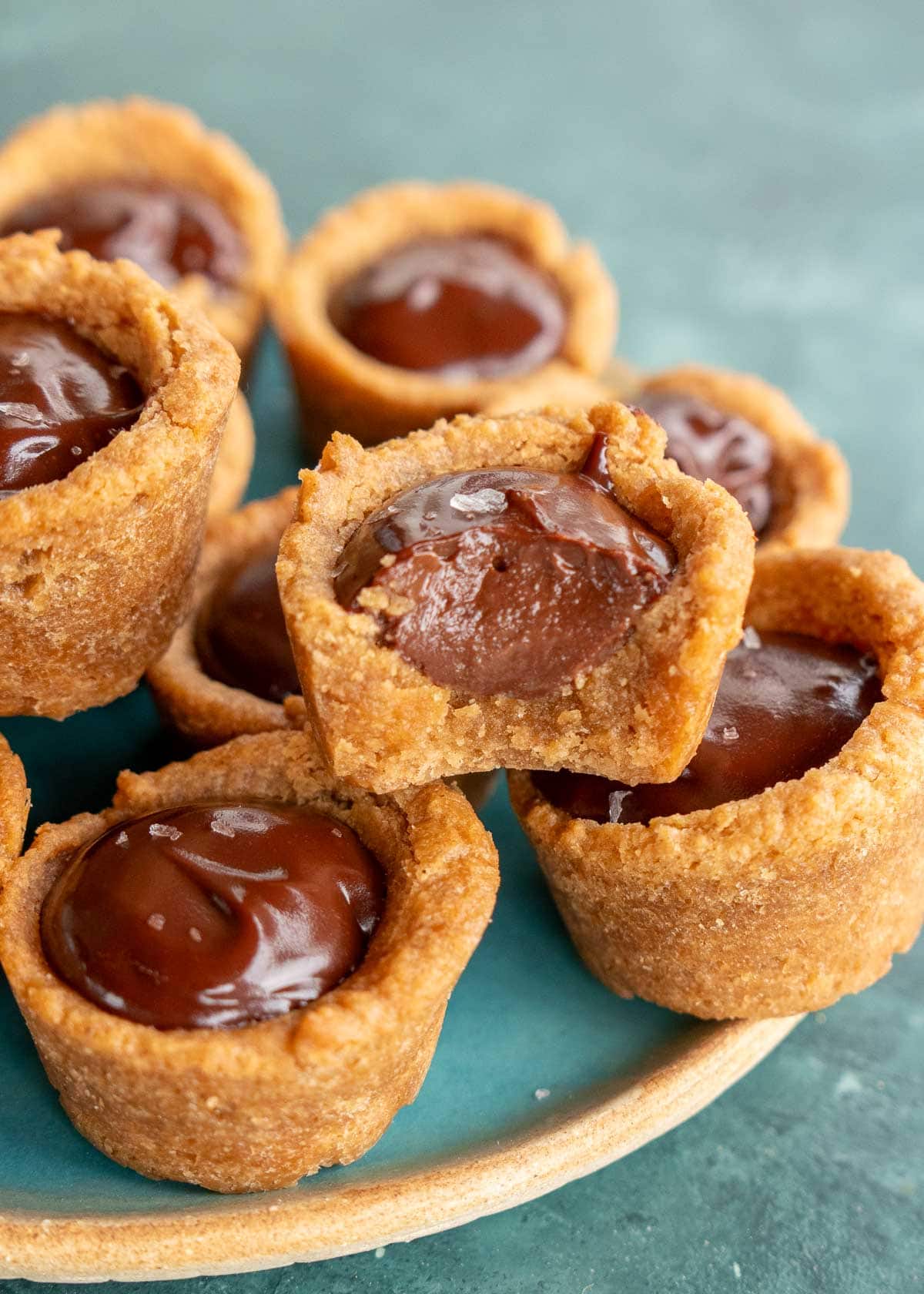 a plate full of chocolate peanut butter cookie cups, including one bitten in half to show the ganache filling