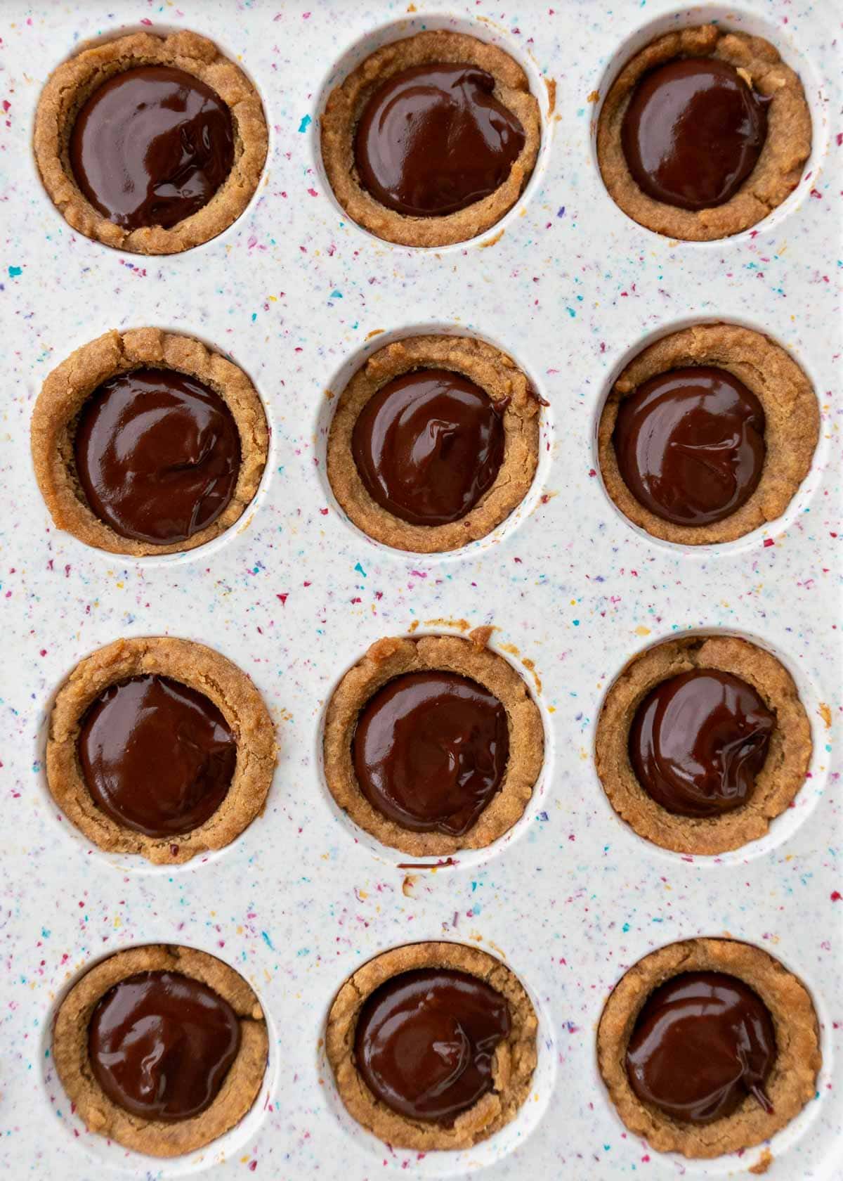 gluten-free peanut butter cookie cups filled with sugar-free chocolate ganache in a mini muffin pan