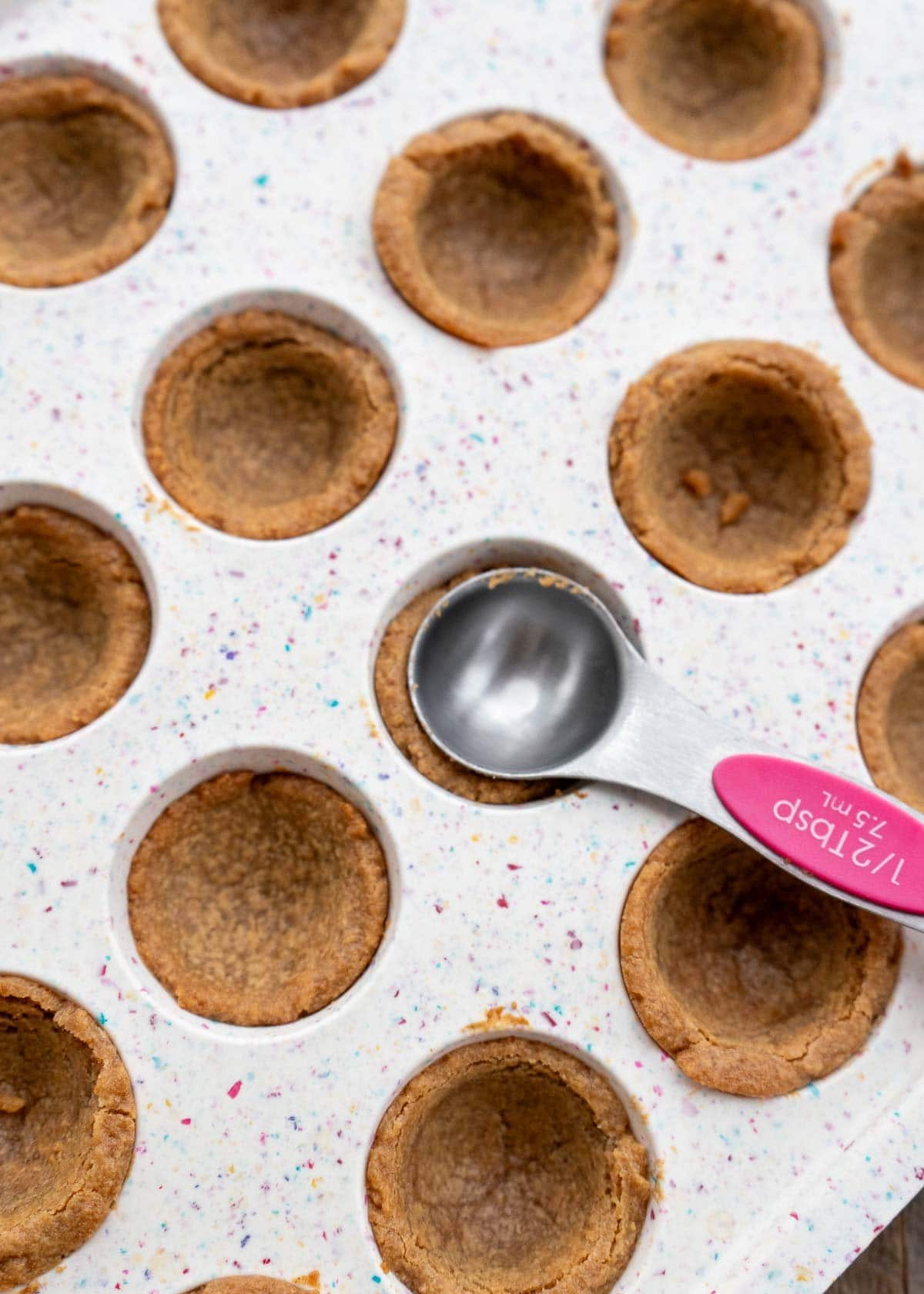 a measuring spoon gently pressing into the cooked cookies to make a deeper well