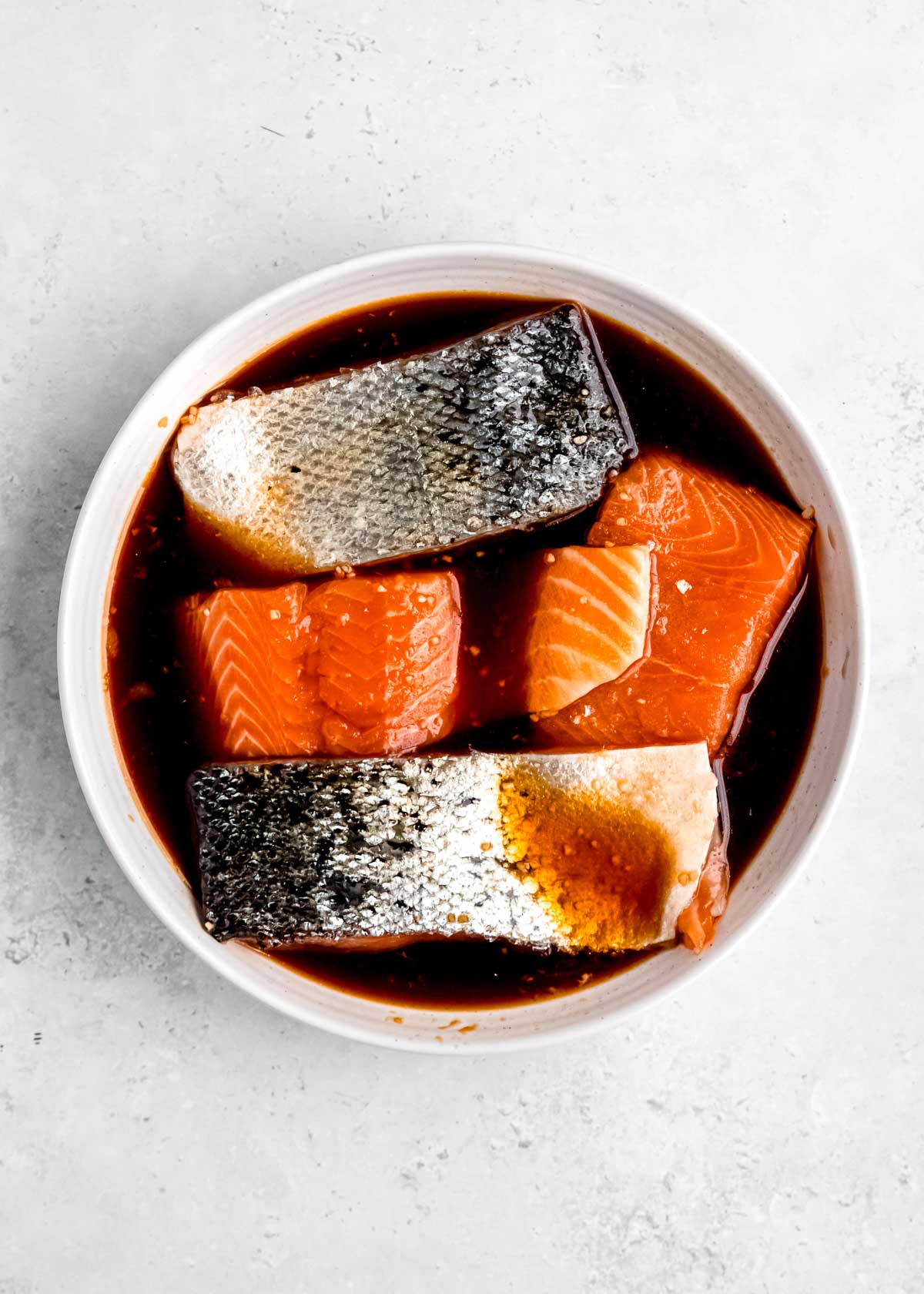 salmon being marinated in white bowl